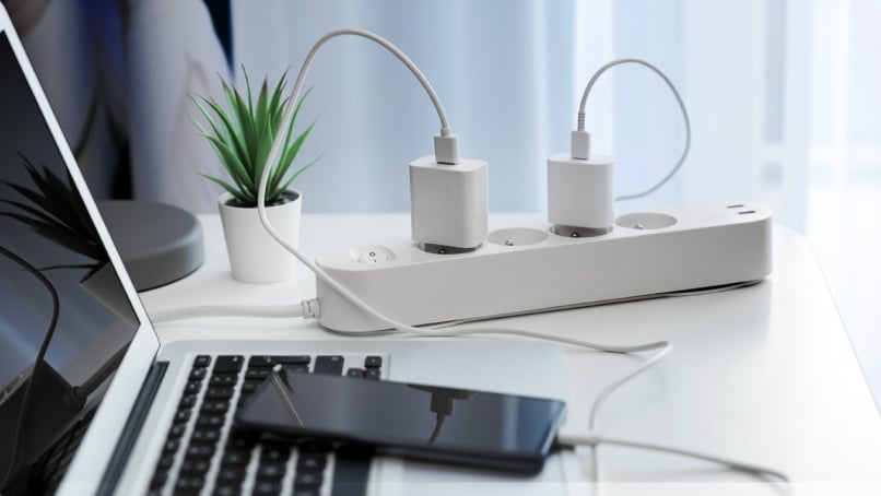 Electrical plug in outlet socket on table connected to laptop and mobile phone.