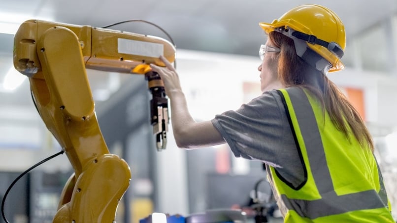 Engineer wearing PPE calibrates a robotic arm in an industrial automation environment.