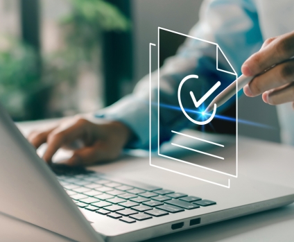 Person's hand pointing to check marked compliant documents in front of a laptop