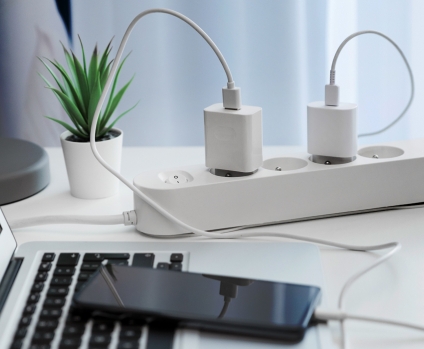 Electrical plug in outlet socket on table connected to laptop and mobile phone.