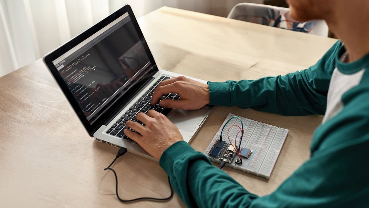Electronic engineer configuring semiconductor board connected to a laptop using software and development tools.