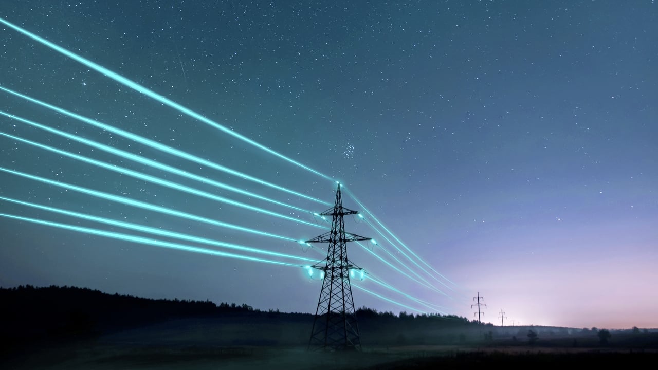 Electricity transmission towers with glowing wires at dusk.